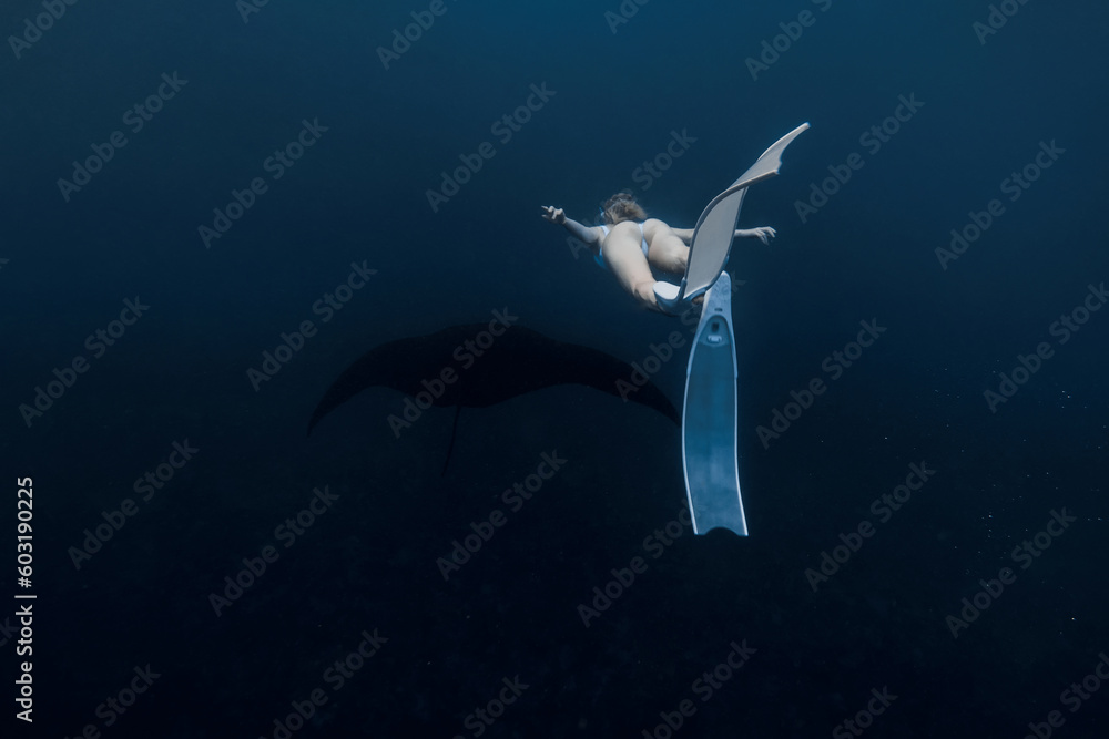 Obraz premium Woman freediver with white fins swim with manta ray. Freediving with manta rays on deep