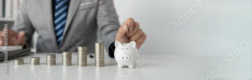 Image of young businessman putting coins into piggy bank ceramic to save money Have a financial plan sufficient to his income for savings and paying off expenses. people and finance concept.