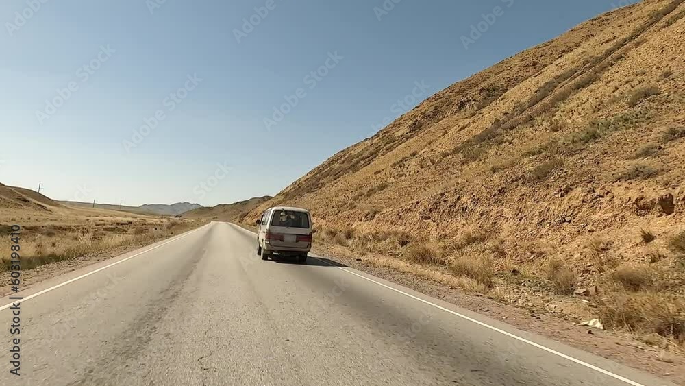 Traveling by minivan in Kyrgyzstan. View of the mountains, green hills, ridges and asphalt road. Beautiful desert mountain landscape. An exciting road adventure. Traveling by minivan in Kyrgyzstan. View of the mountains, green hills, ridges and asphalt road. Beautiful desert mountain landscape. An exciting road adventure.