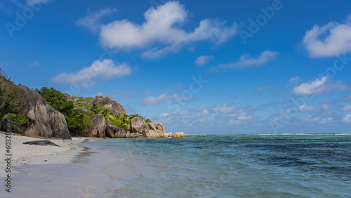 A beautiful beach on a tropical island. Picturesque cliffs with steep smoothed slopes and boulders at the water's edge. Turquoise ocean, white sand, blue sky with clouds. Seychelles. La Digue. 