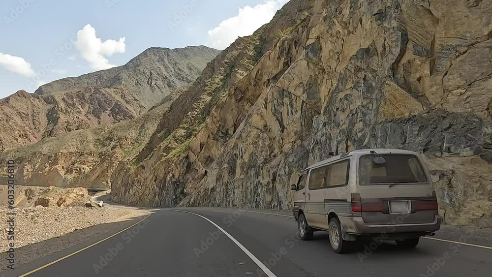Rear view of a minivan driving along an amazing mountain road. View from the car window to the mountains and hills. Traveling by car in Kyrgyzstan. An exciting mountain road adventure. Rear view of a minivan driving along an amazing mountain road. View from the car window to the mountains and hills. Traveling by car in Kyrgyzstan. An exciting mountain road adventure.