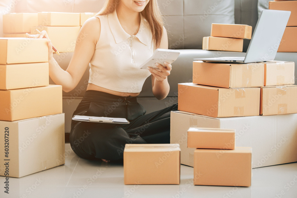 Startup Successful Small Business Owner Young Asian woman sits with laptop, calculator, smartphone and box in home preparing to ship to customer, seller business concept for SME entrepreneurs Startup Successful Small Business Owner Young Asian woman sits with laptop, calculator, smartphone and box in home preparing to ship to customer, seller business concept for SME entrepreneurs