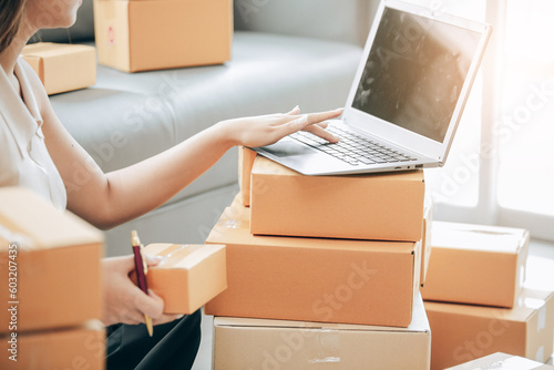 Startup Successful Small Business Owner Young Asian woman sits with laptop, calculator, smartphone and box in home preparing to ship to customer, seller business concept for SME entrepreneurs © ThawKyar