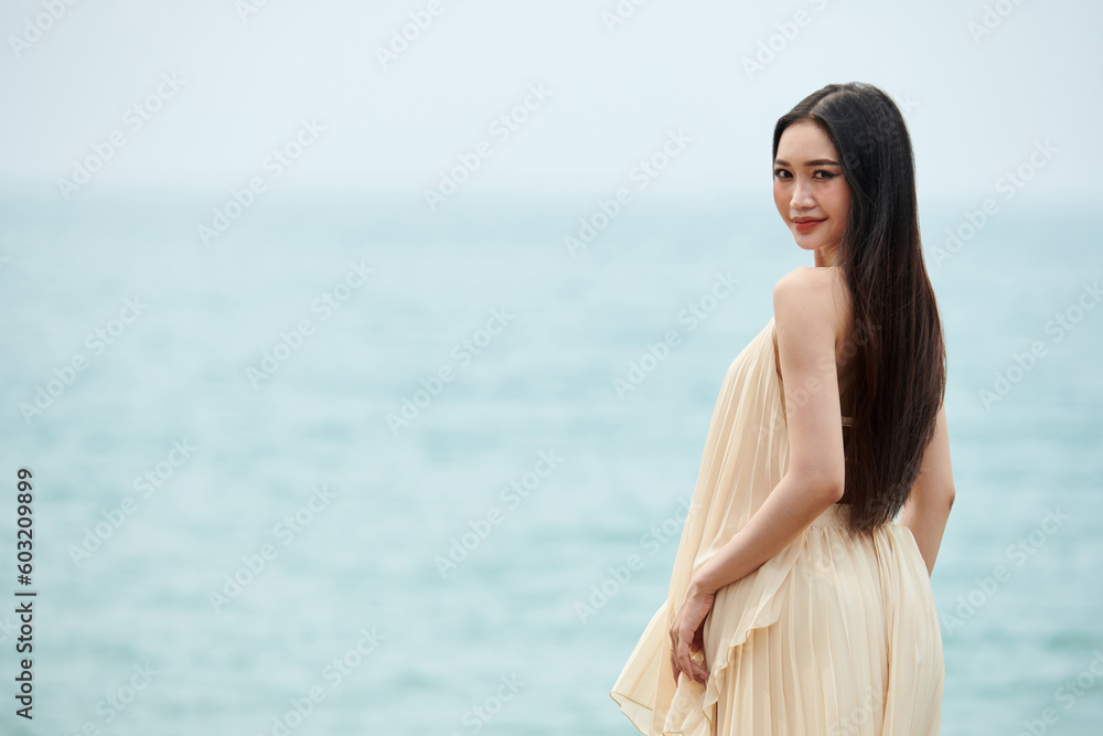 Young woman with long hair standing on beach and turning back to camera Young woman with long hair standing on beach and turning back to camera