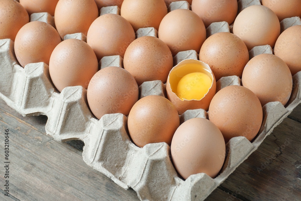 Chicken eggs in a carton box with broken egg half with a yolk