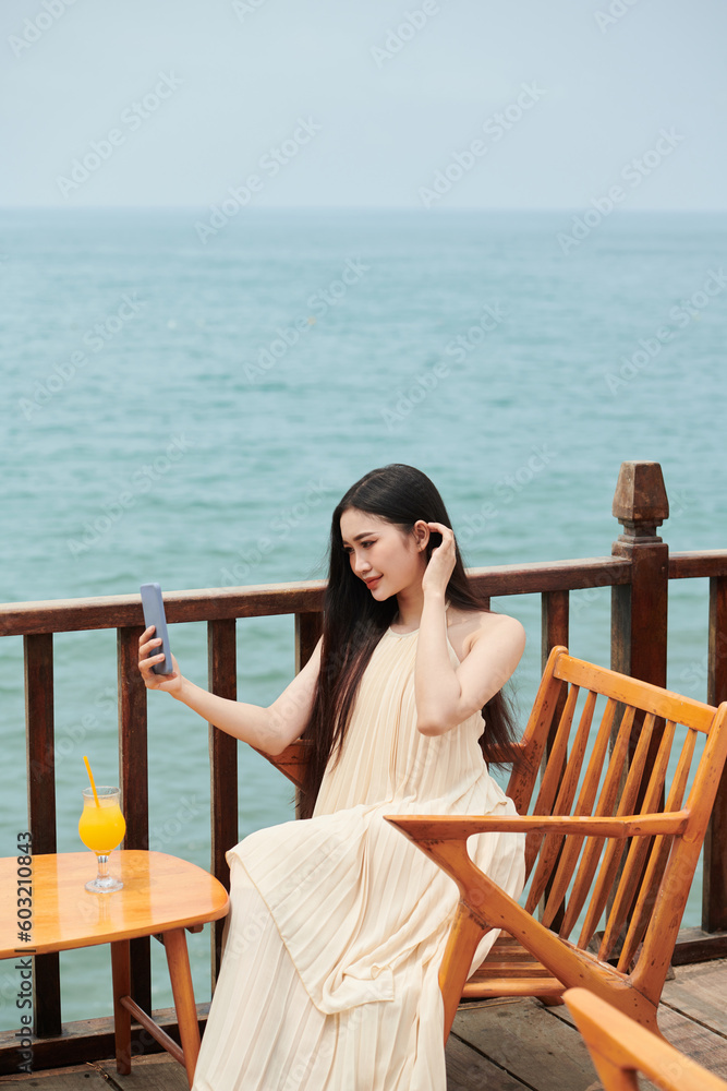 Beautiful young woman with long hair taking selfie at table in coastal cafe Beautiful young woman with long hair taking selfie at table in coastal cafe
