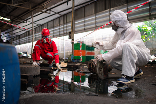 Worker or scientist industry wearing protective safety uniform, white glove and gas mask under cleaning up and lapping spilled oil in factory area to check in laboratory is industry safety concept. photo