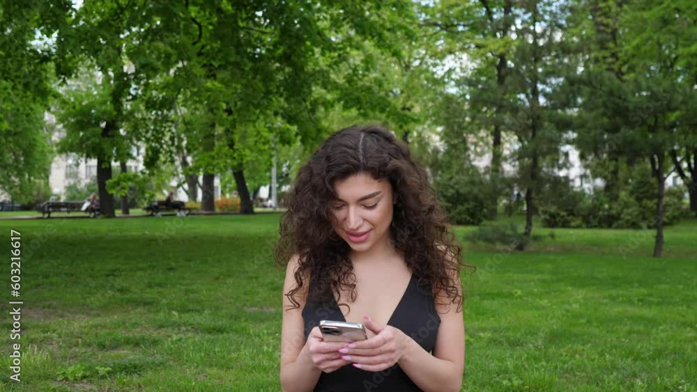 beautiful young brunette woman with curly hair sits in a city park on the lawn and writes a message on the phone 4k beautiful young brunette woman with curly hair sits in a city park on the lawn and writes a message on the phone 4k
