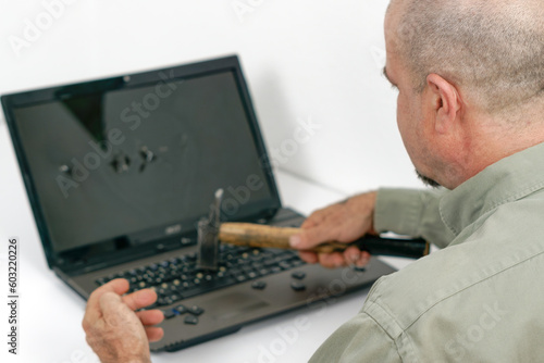 angry man seen in profile breaking a laptop with a hammer , white background and copy space