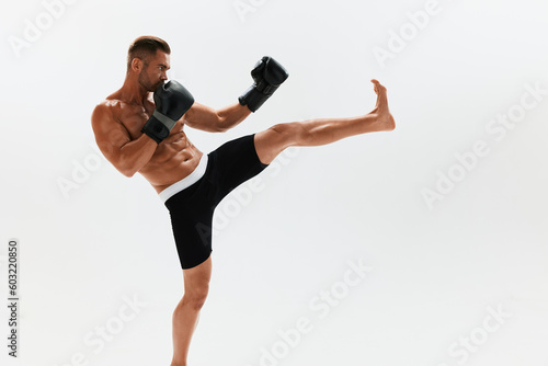 Fototapeta Naklejka Na Ścianę i Meble -  Man athletic bodybuilder poses in boxing gloves with nude torso abs in full-length background, boxing and martial arts. Advertising, sports, active lifestyle, light, competition, challenge concept. 