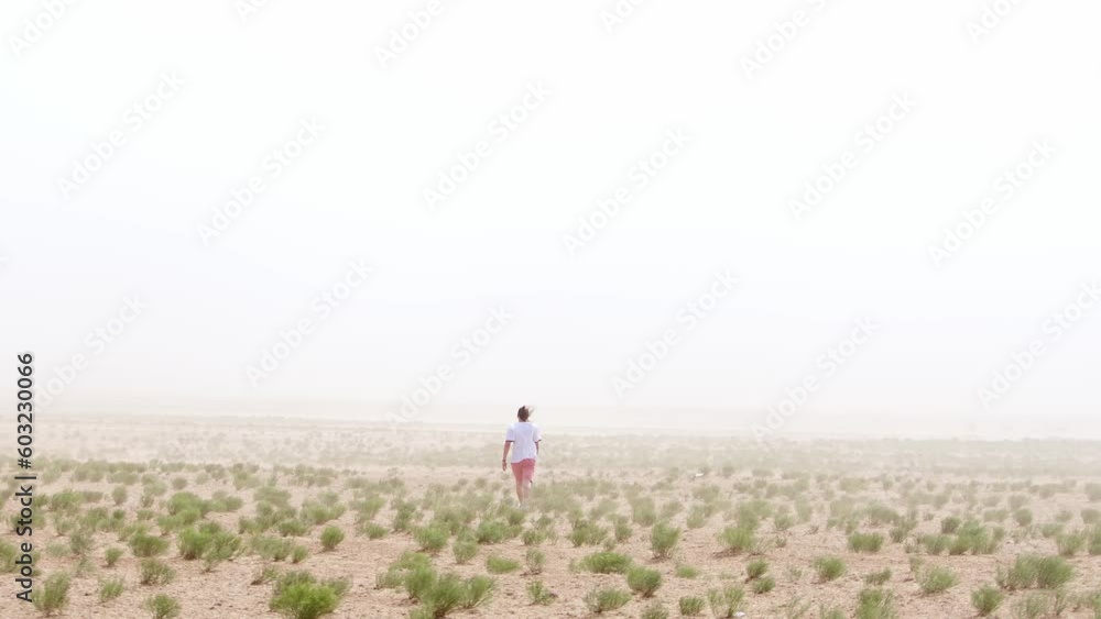 Young man goes through desert overgrown with camel thorns in sandstorm. Back view. Danger concept. Slow motion. Young man goes through desert overgrown with camel thorns in sandstorm. Back view. Danger concept. Slow motion.