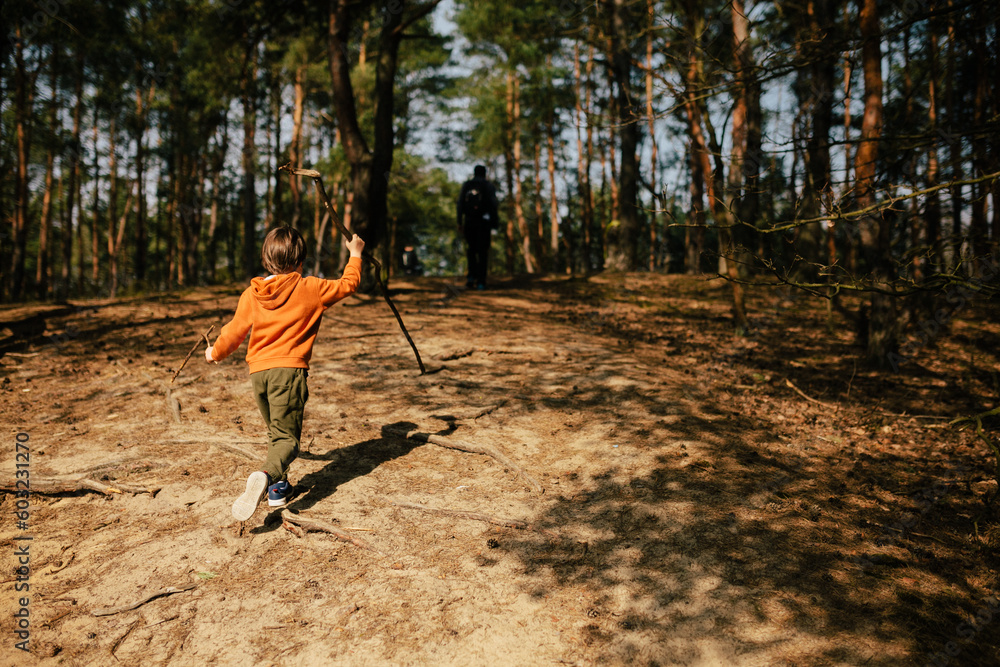 child walking in the spring forest with a long stick