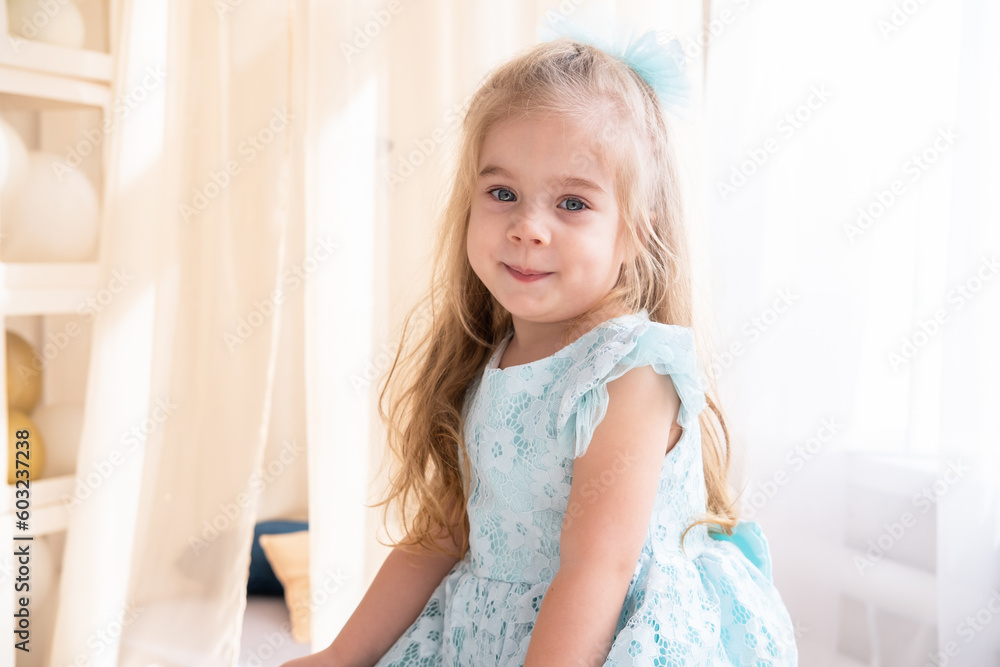 portrait of smiling little girl in blue dress with long blonde hair at home portrait of smiling little girl in blue dress with long blonde hair at home