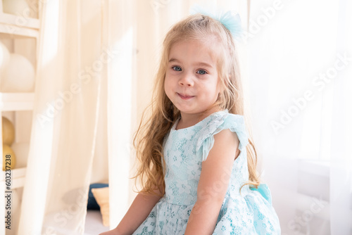 portrait of smiling little girl in blue dress with long blonde hair at home