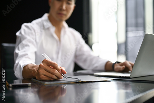 Slika na platnu A businessman working at his desk, writing or taking notes on his notebook