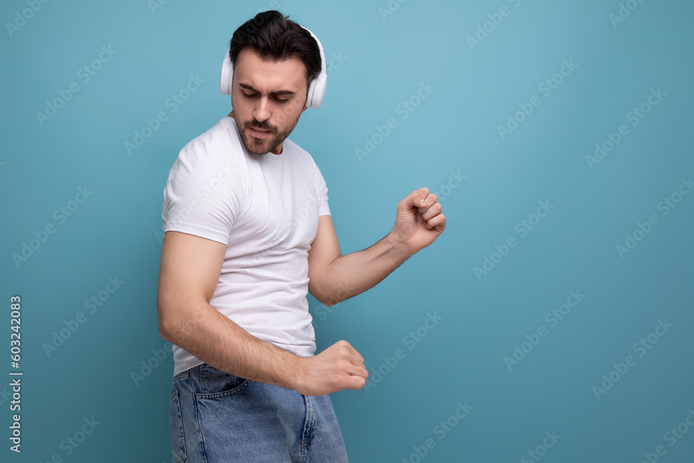 handsome young brutal male millennial brunette in white dances to music in headphones handsome young brutal male millennial brunette in white dances to music in headphones
