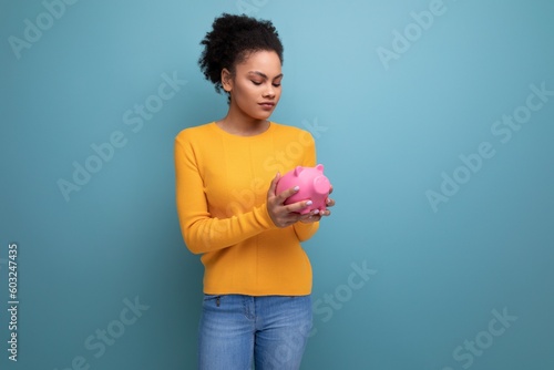 happy young hispanic woman with black curly hair holding a pink piggy bank © Ivan Traimak