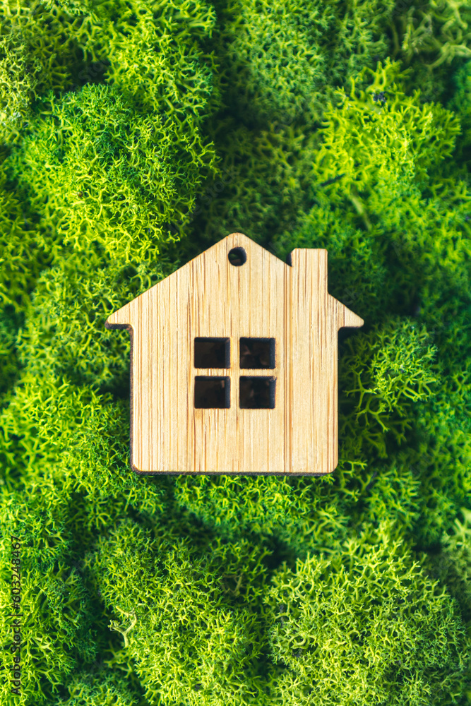 Naklejka premium Miniature wooden house on green moss. concept of selling, insuring or renting real estate. vertical photo