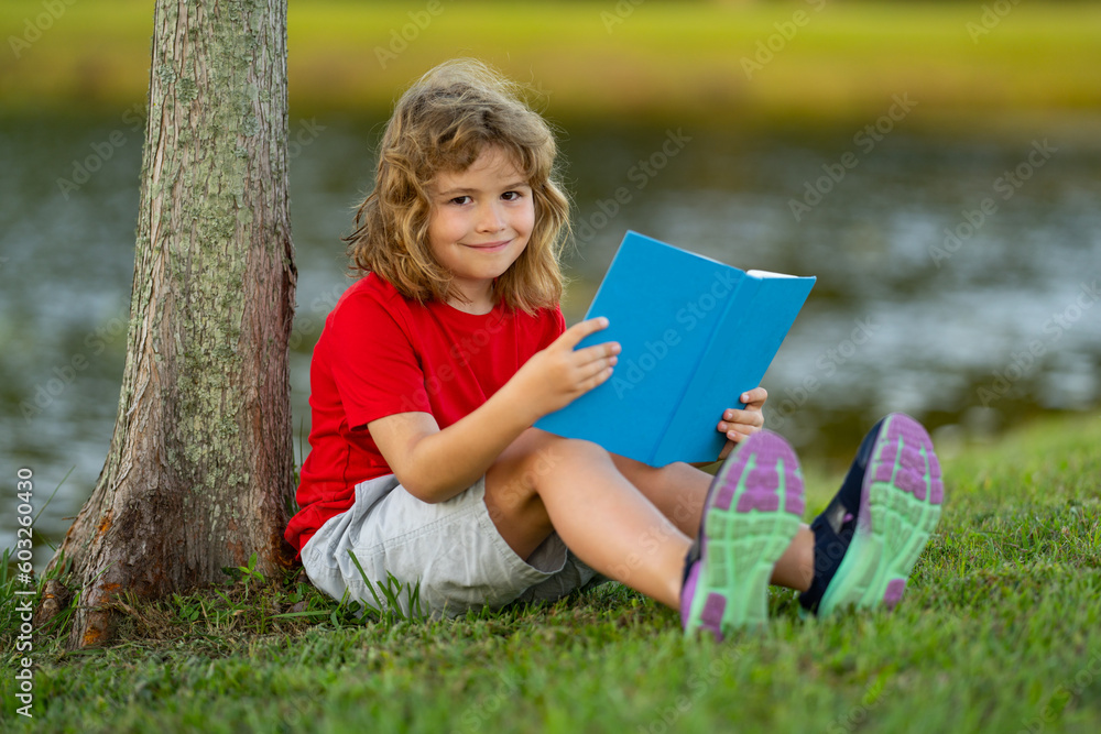 Child with a book. Early education for kids. Summer vacation with book. Outdoor homework. Summer camp with book. Kids learning and education concept. Kid sitting on grass and reading a book. Child with a book. Early education for kids. Summer vacation with book. Outdoor homework. Summer camp with book. Kids learning and education concept. Kid sitting on grass and reading a book.