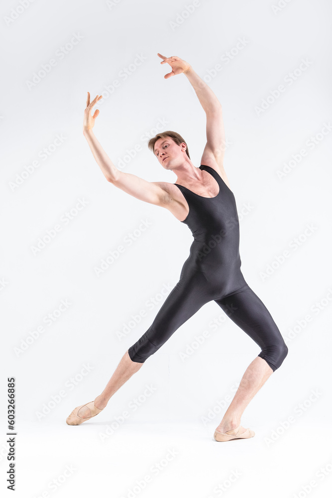 Professional Ballet Dancer Young Caucasian Athletic Man in Black Suit Posing Stretching in Studio On White With Lifted Hands.