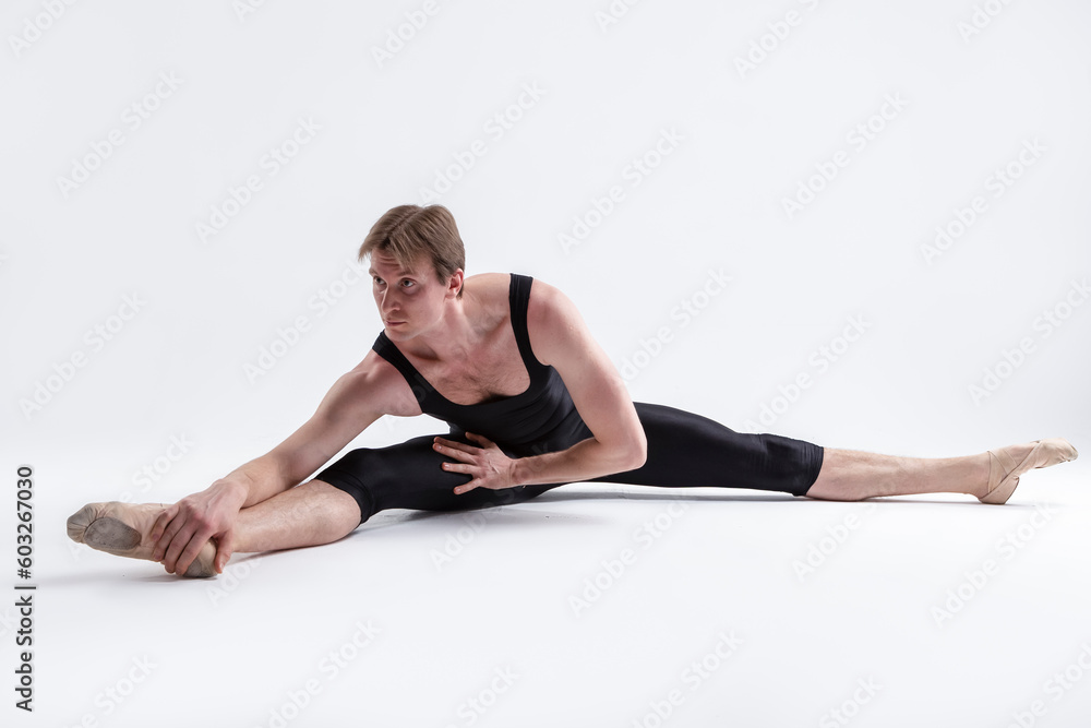 Active Caucasian Relaxed Ballerino Dancer Sitting While Practising Stretching Legs and Body Exercices In Black Sportive Tights in Studio. Active Caucasian Relaxed Ballerino Dancer Sitting While Practising Stretching Legs and Body Exercices In Black Sportive Tights in Studio.