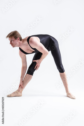 Caucasian Relaxed Ballerino Dancer Sitting While Practising Stretching  Legs and Body Exercices In Black Sportive Tights in Studio.