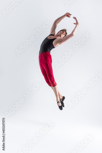 Contemporary Ballet of Young Flexible Athletic Man Posing in Red Tights in Flying Dance Pose With Hands Lifted and Connected in Studio on White.