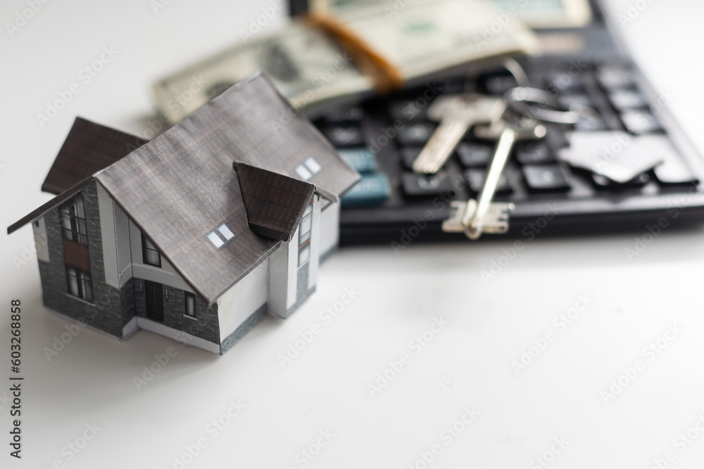 Fototapeta premium A model house sitting with a calculator and twenty dollar bills on a white background with clipping path, mortgage calculator.