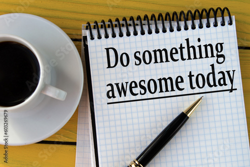 DO SOMETHING AWESOME TODAY - words on a white sheet on a yellow wooden background with a pen and a cup of coffee