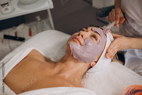 close up of beautiful woman lying with closed eyes and cosmetologist applying facial mask