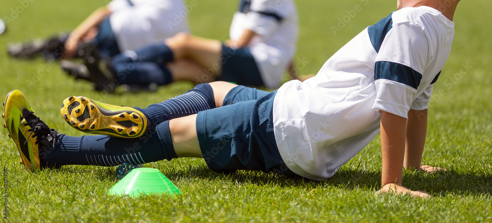 Young boy rolling calf using foam roller at training pitch. School soccer practice unit for young athletes Young boy rolling calf using foam roller at training pitch. School soccer practice unit for young athletes