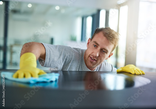 Man with gloves cleaning surface in office, health and hygiene in workplace, janitor at clean desk. Professional cleaner wiping table in workplace, maintenance and disinfectant on cloth for germs. photo