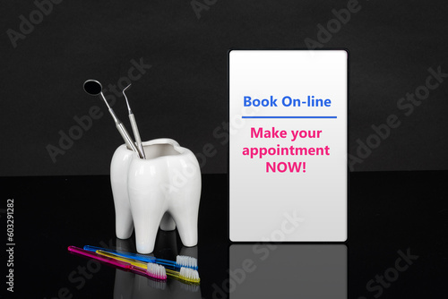 Dentist appointment date or any other dental message on tablet, ceramic tooth with three bright colors toothbrushes and dental tools mock up. Black background.