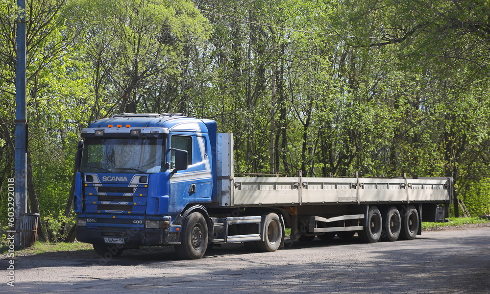 A truck with a long open body is parked on a forest road, Dal'nevostochniy Prospekt, St. Petersburg, Russia, May 2023