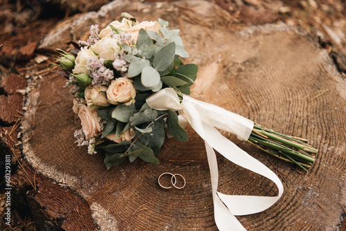 Beautiful wedding bouquet with protea and roses, wedding rings on a forest background