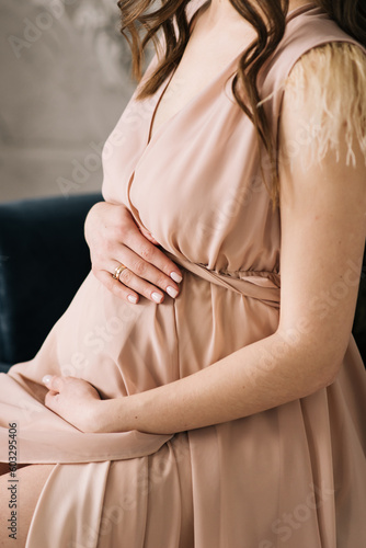 Pregnant girl in a dress hugs her belly