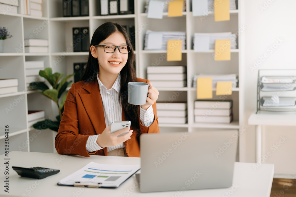 Confident beautiful Asian businesswoman typing laptop computer and digital tablet while holding coffee at office Confident beautiful Asian businesswoman typing laptop computer and digital tablet while holding coffee at office