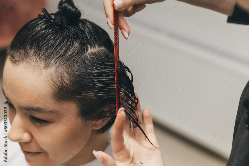 Naklejka premium hairdresser makes a haircut to a woman in the salon. The hairdresser cuts wet hair, combing with a comb. client with short hair. back view