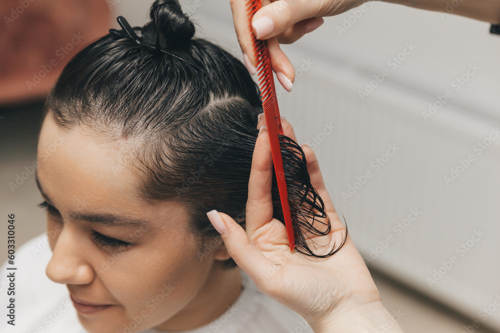 Naklejka premium hairdresser makes a haircut to a woman in the salon. The hairdresser cuts wet hair, combing with a comb. client with short hair. back view