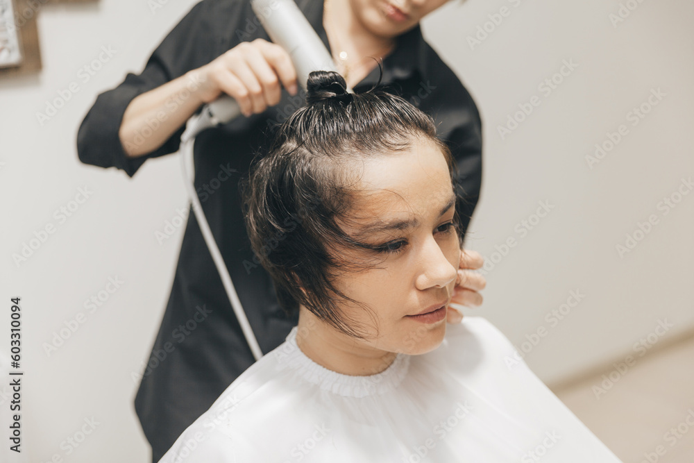 Fototapeta premium Close-up of the hands of a hairdresser drying women's hair with a hairdryer. short haircut and styling