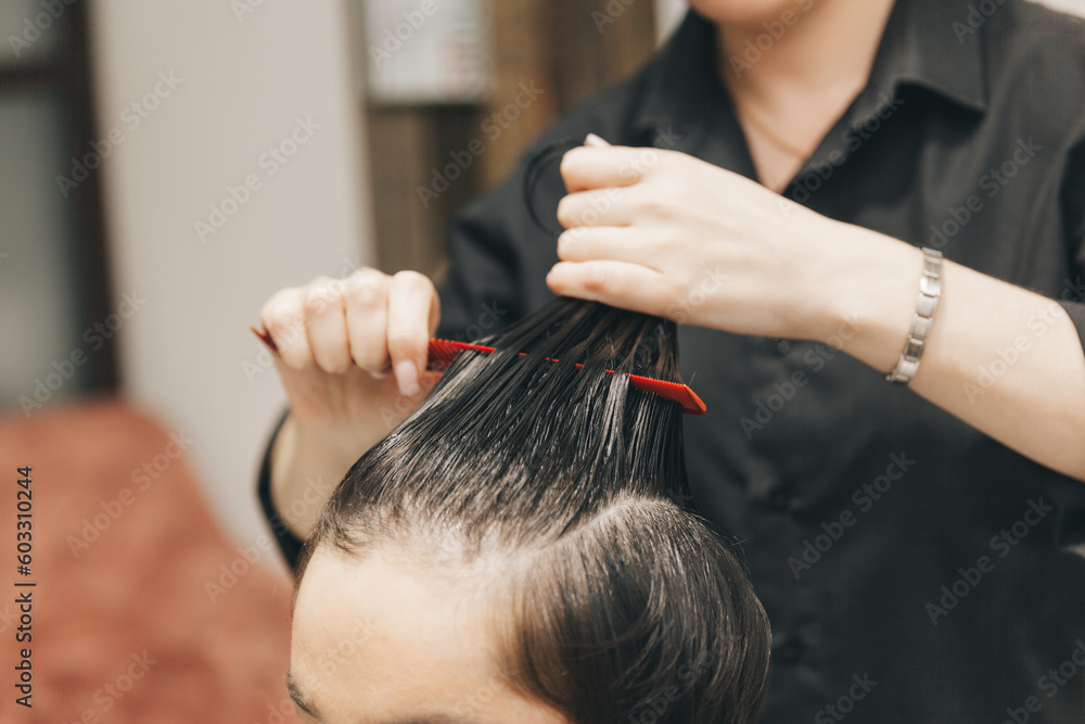 hairdresser makes a haircut to a woman in the salon. The hairdresser cuts wet hair, combing with a comb. client with short hair. back view hairdresser makes a haircut to a woman in the salon. The hairdresser cuts wet hair, combing with a comb. client with short hair. back view