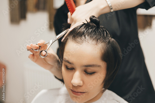 hairdresser makes a haircut to a woman in the salon. The hairdresser cuts wet hair, combing with a comb. client with short hair. back view