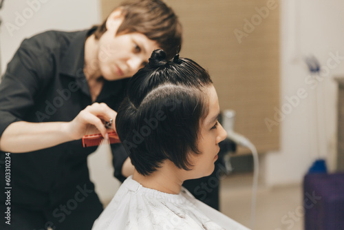 hairdresser makes a haircut to a woman in the salon. The hairdresser cuts wet hair, combing with a comb. client with short hair. back view