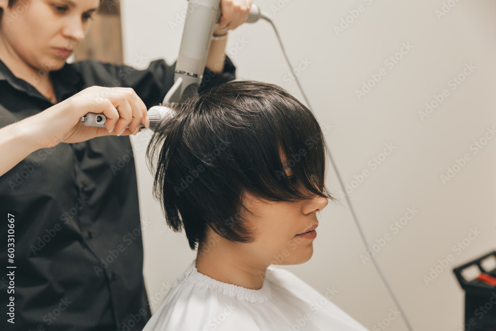 Fototapeta premium Close-up of the hands of a hairdresser drying women's hair with a hairdryer. short haircut and styling