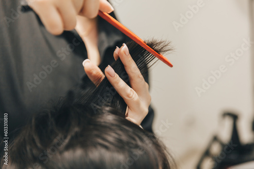 hairdresser makes a haircut to a woman in the salon. The hairdresser cuts wet hair, combing with a comb. client with short hair. back view