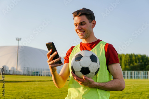 Portrait of young smiling man football player holding soccer ball and using smartphone photo