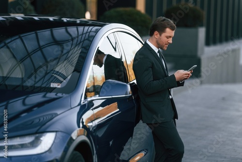 Using smartphone. Businessman is standing near his car outdoors © standret