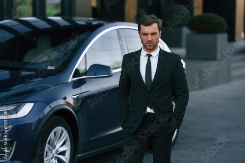 In suit and tie. Businessman is standing near his car outdoors © standret