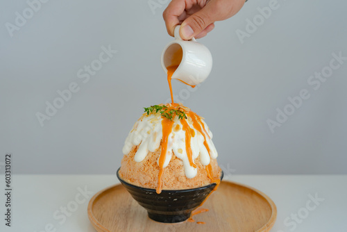 Japanese shaved ice dessert , Hand pouring sweet Thai tea sauce on whipping cream. Served with milk tea kakigori bingsu topped with almond slide condensed milk. Traditional summer dessert in Japan.