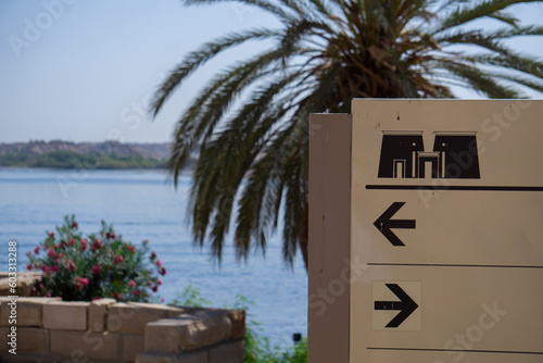 Cartello di un museo egizio che indica le direzioni di ingresso, con una palma, l'oleandro e il fiume Nilo sullo sfondo photo
